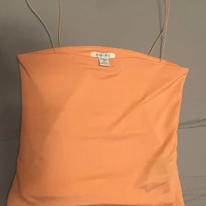 Persikofärgad topp  - Säljer en söt persikofärgad tubtopp från Amisu. Den är perfekt för sommardagar och har smala axelband som ger en stilren look. Materialet är mjukt och bekvämt. Passar perfekt med jeans eller kjol!