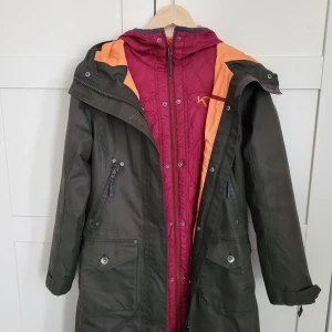 KariTraa parkas  - Höstparkas med feminin design. Många praktiska fickor, midjeåtdragning och justerbara muddar. Det finns innerjacka att ta loss i fin vinröd färg