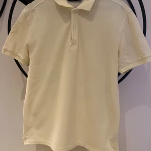 Pikétröja  - Ljusgul piketröja från J Lindeberg i storlek L. Har en liten fläck på framsidan av tröjan, se bild. Har ej försökt att ta bort fläcken ännu, därav det låga priser