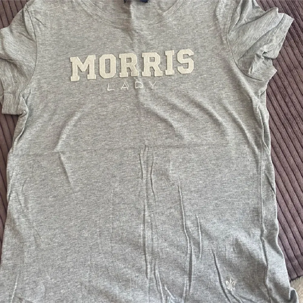 Säljer en snygg grå t-shirt från Morris Lady. Den har korta ärmar och ett stilrent tryck med 'MORRIS LADY' på framsidan. Perfekt för en avslappnad vardagslook. Passar bra till jeans eller shorts!. T-shirts.