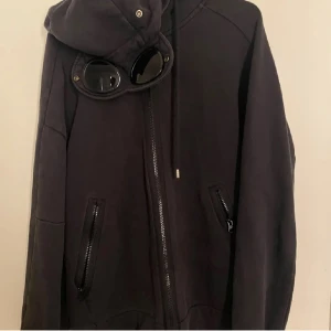 Svart cp company zip hoodie - Den är i bra skick bara lite urtvättad är medium men passar L. Inga hål eller skador på den. Är öppen för o byta mot tex stone island eller liknande märken. Priset är prutat och klart