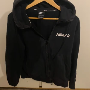 Svart hoodie från Nike Air - Säljer en svart hoodie från Nike Air med dragkedja och huva. Den har en vit Nike Air-logga på bröstet och är tillverkad i ett mjukt material. Perfekt för en avslappnad stil. Priset kan diskuteras där vi båda är glada