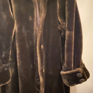 Brun pälsjacka med knappar - Säljer en elegant brun pälsjacka med stora knappar och bred krage. Jackan har långa ärmar och en mjuk, lyxig känsla. Perfekt för att hålla sig varm och stilren under kyliga dagar.