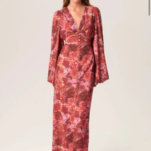 Blommig långklänning från Adoore - Säljer en vacker blommig långklänning från Adoore i röd och rosa nyans. Klänningen har långa ärmar och en v-ringad design med knappar framtill. Perfekt för en elegant look. Storlek 38 helt ny med prislapp. Aldrig använd❤️