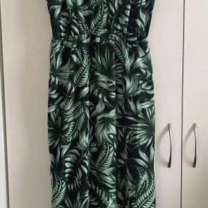 Grön mönstrad långklänning - Snygg långklänning med grönt bladmotiv på svart bakgrund. Klänningen har smala axelband och en bekväm passform som passar perfekt för varma dagar. Perfekt för en somrig look!