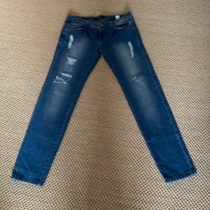 Blå jeans från Sinsay - Snygga blå jeans från Sinsay med slitna detaljer och en hjärtformad knapp. De har en klassisk femficksdesign och en bekväm passform. Perfekta för en avslappnad stil.