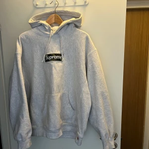 Grå hoodie från Supreme - Säljer en grå hoodie från Supreme med klassisk logga på bröstet. Den har en stor ficka framtill och justerbar huva med dragsko. Perfekt för en avslappnad stil. Storlek Large 