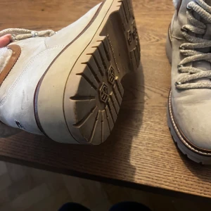 Hilfiger Beige läderboots med snörning - Snygga beige boots med snörning och vadderad insida i fuskpäls. Skorna har en robust sula och detaljer i brunt läder. Perfekta för kyligare väder med en stilren design.