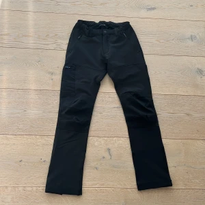 Svarta byxor från Everest - Snygga svarta byxor från Everest med dragkedja på fickorna. Perfekta för utomhusaktiviteter med en bekväm passform och elastisk midja. Byxorna har en stilren design och är gjorda i ett slitstarkt material.