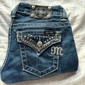 Miss Me jeans  - Snygga blå jeans från Miss Me med låg midja och bootcut-stil. De har dekorativa detaljer som nitar och broderier på bakfickorna. Sömen längst ned är uppsprättad. Midjemått: 34 innerbenslängd: 78