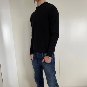 Svart stickad tröja i ull från SAMSØE - Säljer en stilren svart tröja med långa ärmar från SAMSØE. Perfekt för en enkel och klassisk look. Tröjan har ribbade muddar vid ärmslut och nederkant. Skick 8.5/10. Modellen är 173 och den är för liten. Passar xs