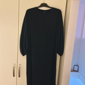 Svart långklänning - Elegant svart långklänning med långa ärmar och rund halsringning. Perfekt för en stilren och klassisk look. Klänningen har en enkel design som gör den lätt att matcha med olika accessoarer.