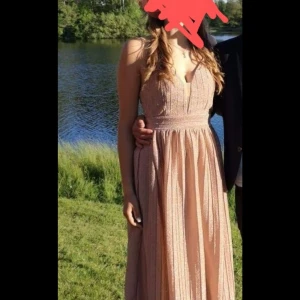 Champagnefärgad balklänning - Jag är 182 och den var bra längd med klackar till. Elegant champagnefärgad långklänning med v-ringad hals och ärmlös design. Perfekt för en somrig bal eller fest. Klänningen har en fin struktur och faller vackert. 