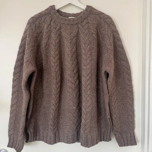 Brun stickad tröja från Hope - Säljer en snygg brun stickad tröja från Hope. Tröjan har ett klassiskt flätmönster och långa ärmar med ribbade muddar. Perfekt för kyliga dagar och ger en stilren look.