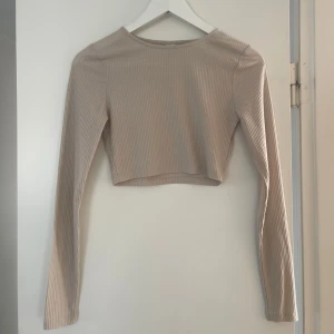 Beige ribbad croppad topp - Säljer en stilren beige ribbad croppad topp med långa ärmar. Använd ett fåtal gånger!