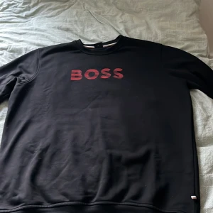 Svart tröja från Boss - En svart boss tröja med röd text. 10/10 skick använd 2-3 gånger. Materialet är väldigt skönt och snyggt passar bra med jeans. Storlek xl men funkar också för L. Pris kan diskuteras vid snabbaffär.