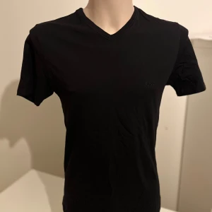 Svart t-shirt från Hugo Boss - Snygg svart t-shirt från Hugo Boss med v-ringning. Perfekt för en stilren look. T-shirten är kortärmad och har en diskret logga på bröstet.