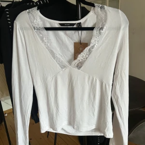 Vit spetsdetaljerad topp från Vero Moda - Säljer en vit långärmad topp från Vero Moda med v-ringning och spetsdetaljer runt halsen. Perfekt för en stilren look. Toppen är i storlek M men var stor i storleken och passar därför inte mig. Skulle säga att den är mer som en L. Aldrig använd med lappen kvar