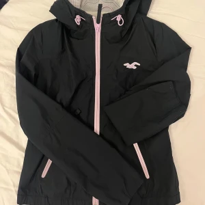 Svart vindjacka från Hollister - Säljer en svart vindjacka från Hollister. Jackan har en justerbar huva och långa ärmar. Perfekt för blåsiga dagar. 🖤