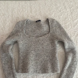 Grå stickad tröja från Gina Tricot - Säljer en stilren grå stickad tröja från Gina Tricot. Tröjan har en fyrkantig halsringning och är ribbad med långa ärmar. Perfekt för kyligare dagar.