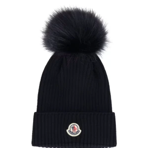 Svart ribbad mössa med pälsboll från Moncler - Snygg svart ribbad mössa från Moncler med en stor pälsboll på toppen. Mössan har en broderad logotyp framtill och är perfekt för kyliga dagar. Jag har fått den i present, använder den inte särskilt mycket. 