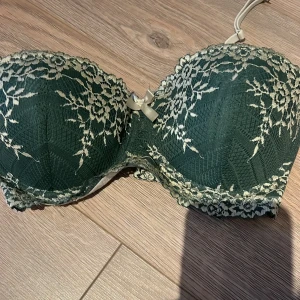 Grön spets-bh med rosett - Snygg grön bh med vacker spetsdetalj och en söt rosett framtill. Den har vadderade kupor och justerbara axelband för bästa passform. Perfekt för att känna sig extra fin!