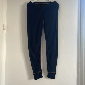 Svarta underställsbyxor frånL.Brador - Snygga svarta underställsbyxor  från L.Brador med kontrasterande orange sömmar. Tillverkade i 100% polyester för en bekväm passform. Perfekta för en aktiv livsstil.