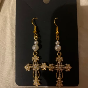Guldörhängen med kors och pärlor - Egengjorda guldörhängen med korsdesign dekorerade med vita pärlor. Perfekta för att ge en stilfull touch till din outfit. Hängande modell med krokfäste.