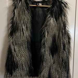 Svart och grå pälsväst - Snygg och trendig svart och grå pälsväst med ett mönster som ger en cool look. Perfekt för att lägga till lite extra stil till din outfit. Västen är ärmlös och har en mjuk insida.🖤🖤