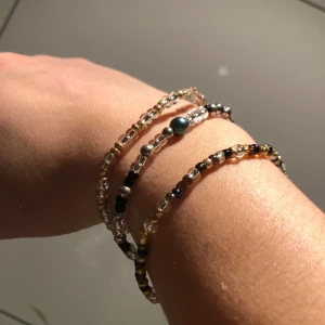 Flerfärgade pärlarmband - Säljer tre stilrena armband med små pärlor i olika färger som silver, guld och svart. Varje armband har en unik design med en större pärla som detalj. Perfekt för att ge en elegant touch till din outfit. 150 för alla, 50 för ett