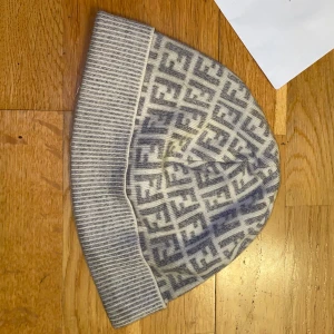 Grå och vit mössa från Fendi - Snygg mössa från Fendi i grått och vitt med ett stilrent mönster. Perfekt för att hålla värmen med stil under kyliga dagar.