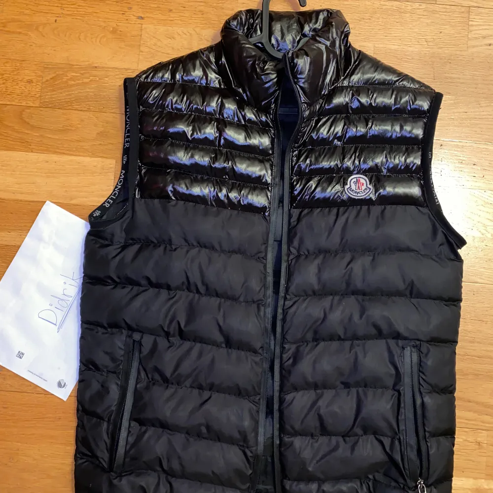 Snygg svart dunväst från Moncler med dragkedja och hög krage. Perfekt för kyligare dagar och ger en stilren look. Moncler-logga på bröstet och diskreta fickor med dragkedja.. Takit.