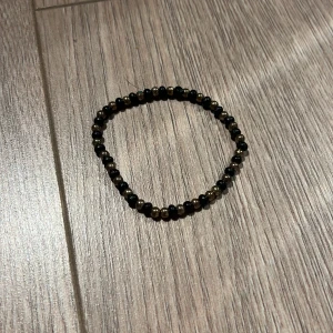 Svart och guld pärlarmband - Elegant armband med svarta och guldiga pärlor. Perfekt för att ge en stilren touch till din outfit. Elastiskt band för enkel passform.