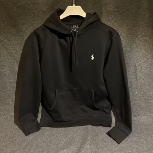 Ralph lauren hoodie svart  - Snygg svart hoodie från Polo Ralph Lauren med klassisk logga på bröstet. Tröjan har en känguruficka och justerbar huva med snören. Perfekt för en stilren och bekväm look. Skick 8/10, Stl Xs 