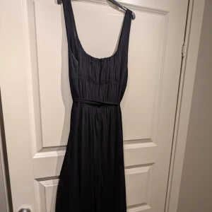 Svart långklänning från Vila - Elegant svart långklänning från Vila med breda axelband och en smickrande passform. Klänningen har en dragkedja i ryggen och ett fint fall som ger en stilren look. Perfekt för speciella tillfällen.