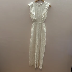 Vit one pice - Säljer en elegant vit klänning med volangdetaljer på axlarna. Klänningen är ärmlös och har en fin struktur i tyget som ger en unik look. Perfekt för somriga tillfällen.