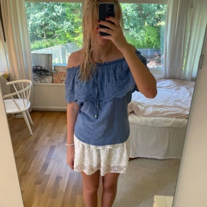 Blå off-shoulder topp med spetsdetaljer - Säljer en superfin blå off-shoulder topp med spetsdetaljer. Toppen har en lös passform och är perfekt för sommaren. Den är ärmlös och har en söt volangkant som ger en romantisk touch. Perfekt för både vardag och fest!