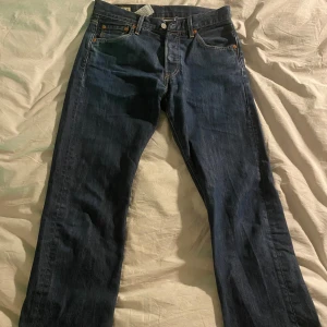 Levi's 501 jeans - Säljer ett par klassiska Levi's 501 jeans i mörkblå denim. De har en straight passform och är i bra skick. Perfekta för en avslappnad stil och funkar året runt. Jeansens ikoniska design med fem fickor och knappgylf gör dem tidlösa och mångsidiga.