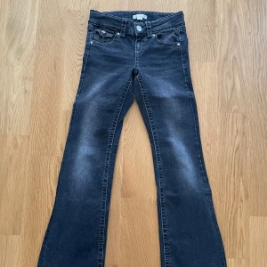 Svarta jeans från Gina Tricot - Säljer ett par snygga mörkgrå jeans från Gina Tricot. De har en klassisk femficksdesign med knappar och dragkedja fram. Jeansen har bootcut och är perfekta för både vardag och fest. De är i bra skick och redo för en ny ägare!
