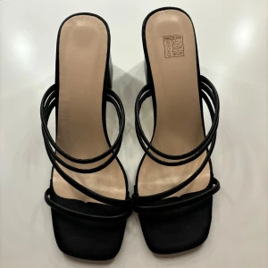 Svarta sandaler med klack - Säljer ett par eleganta svarta sandaler med klack. De har tunna remmar som korsar över foten och en fyrkantig tå. Perfekta för en utekväll eller fest! Helt oanvända!