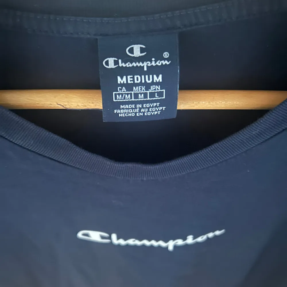 Snygg mörkblå t-shirt från Champion med logga på bröstet och längs ärmarna. Perfekt för en sportig look eller avslappnad stil. Tillverkad i mjukt material för extra komfort.. T-paidat.