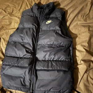 Nike väst  - Säljer en svart dunväst från Nike med dragkedja framtill. Västen har en klassisk design med Nike-logga på bröstet och är perfekt för kyligare dagar. Den är lätt och bekväm att bära. Endbart testar den någon gång men gillade inte hur den satt på mig så den är i helt nyskick. Ganska stor i storleken skulle säga att den passar till 165-175 
