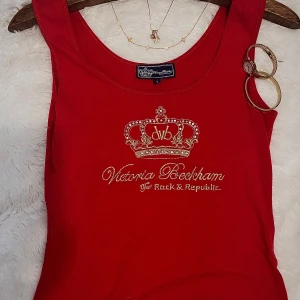 röd linne, victoria Beckham💋✨ - Snygg röd linnetopp från Victoria Beckham for Rock & Republic med ett guldfärgat kronmotiv och text på framsidan. Perfekt för att ge en touch av glamour till din outfit.
