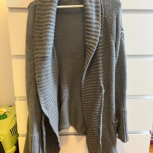 Grå stickad kofta från Odd Molly - Säljer en mysig grå stickad kofta från Odd Molly. Koftan har långa ärmar och en öppen design med ett broderat märke på ärmen. 