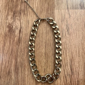 Guldfärgat halsband med kedjedesign - Snyggt guldfärgat halsband med kraftiga länkar i kedjedesign. Perfekt för att ge en trendig touch till din outfit. Halsbandet har en justerbar kedja för att passa olika längder.