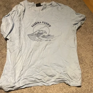 Ljusblå t-shirt från Fuze - Säljer en ljusblå t-shirt från Fuze med tryck av en våg och texten 'Pauena Point Surf Life' på framsidan. T-shirten är kortärmad och tillverkad i bomull, perfekt för en avslappnad stil. Snygg att ha till en par shorts eller en avslappnad oversized sov tröja! Pris kan alltid diskuteras, skriv till mig för övriga frågor eller bilder!