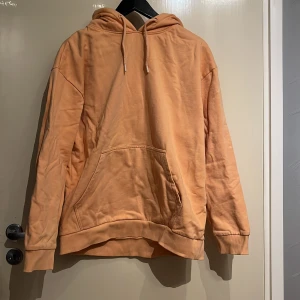 Persikofärgad hoodie från 157 - Säljer en snygg persikofärgad hoodie från 157. Den har en klassisk design med en stor ficka fram och justerbar huva med dragsko. Perfekt för en avslappnad stil.