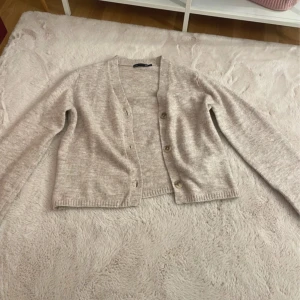 Beige kofta  - Säljer en stilren beige kofta från 157. Den har en klassisk design med knappar framtill och långa ärmar. Den är helt ny i storlek S 