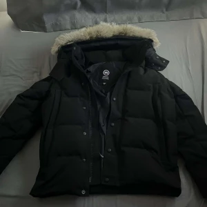 Canada Goose Wyndham - Säljer en svart dunjacka från Canada Goose med pälskantad huva. Jackan har en klassisk design med dragkedja och knappar framtill. Perfekt för kalla vinterdagar. Använd 5-10 gånger går att ta av och på pälsen med en zipper. den har inga defekter ny pris 10.000kr mitt pris 3200kr. Storlek S passar mig perfekt är 180 väger 60kg. Pris går att diskuteras