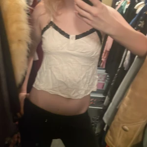 Vit spetskantad topp från Shein - Säljer en söt beige topp från Shein med svarta spetsdetaljer vid axelbanden. Toppen är ärmlös och har en lätt croppad passform. Perfekt för varma dagar eller som ett lager under en jacka.